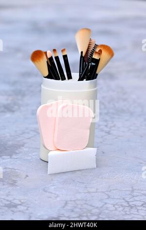 closeup the bunch white brown makeup kit brush with sponge ball in the plastic box over out of focus grey brown background. Stock Photo