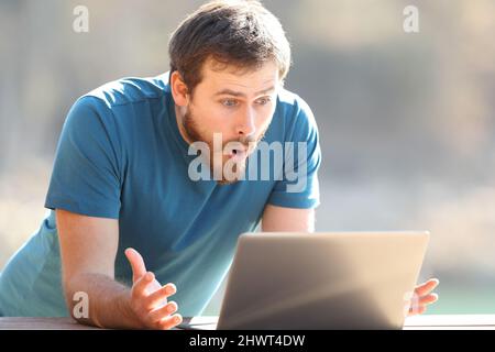 Amazed man checking laptop content outdoors a sunny day Stock Photo
