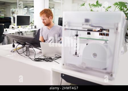 Working on getting some models printed. A shot of a young man printing his designs on a 3D printer. Stock Photo