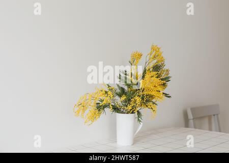 Spring flowers composition. Yellow mimosa flowers on white background in home interior. Stock Photo