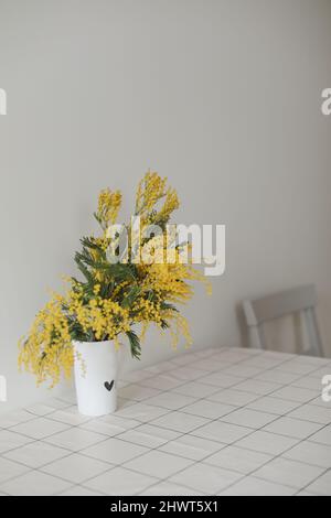 Mimosa branches in a glass vase on the table. Stock Photo