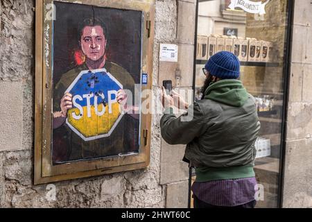 Barcelona, Spain. 07th Mar, 2022. A person is seen taking a photo of the collage depicting Ukraine's president Zelensky calling for an end to the Russian invasion is seen in Plaza de Sant Jaume.The Italian artist TvBoy residing in Barcelona places a collage representation of the Ukrainian president Volodímir Zelensky asking for the end of the Russian occupation in one of the accesses to the Plaza Sant Jaume. (Photo by Paco Freire/SOPA Images/Sipa USA) Credit: Sipa USA/Alamy Live News Stock Photo