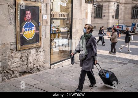 Barcelona, Spain. 07th Mar, 2022. A woman with a suitcase is seen looking at the collage depicting Ukraine's President Zelensky calling for an end to the Russian invasion seen in Plaza de Sant Jaume.The Italian artist TvBoy residing in Barcelona places a collage representation of the Ukrainian president Volodímir Zelensky asking for the end of the Russian occupation in one of the accesses to the Plaza Sant Jaume. (Photo by Paco Freire/SOPA Images/Sipa USA) Credit: Sipa USA/Alamy Live News Stock Photo