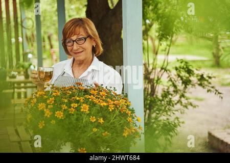 Happy aged woman enjoying tea on blooming terrace Stock Photo
