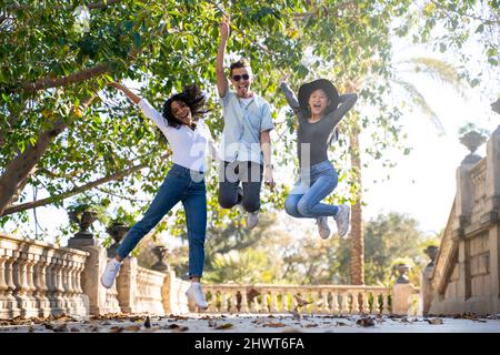 Three friends having fun jumping in the street looking at the camera Stock Photo