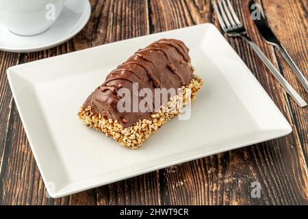 Dessert Cake from Malaga on wooden table. Cake with banana inside, covered with chocolate sauce and hazelnuts. Stock Photo