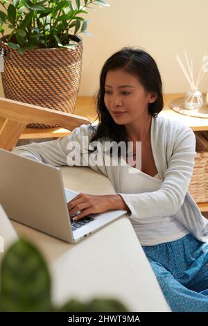 Smiling young woman working on laptop at home, coding or testing new product Stock Photo