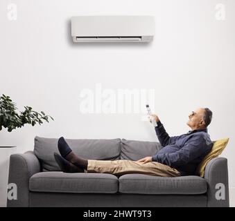 Mature man on a sofa putting the air conditioning on isolated on white backgrounda Stock Photo