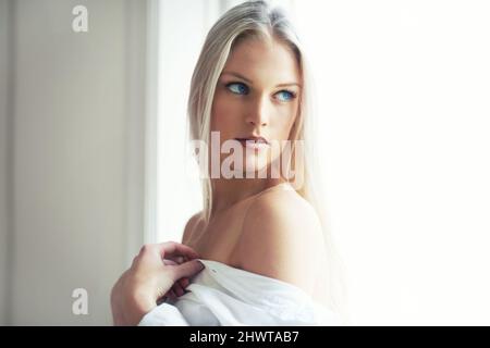 Beauty in the bedroom sun. An attractive young woman standing in her bedroom with her shirt hanging off her shoulders. Stock Photo