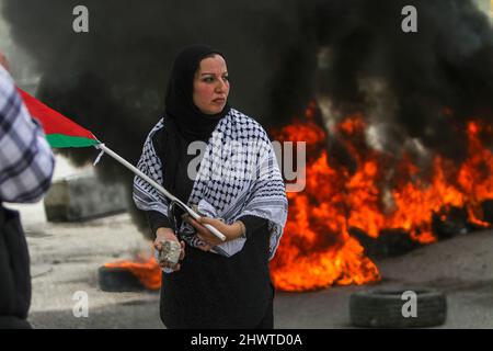 Gaza, Palestine. 07th Mar, 2022. A Palestinian woman holds the Palestinian flag near the burning tires during the protest. Ahead of International Women's Day, Palestinian women protested against the Israeli settlements and their expansion in the West Bank, near the Israeli settlement of Homesh in the occupied West Bank. Credit: SOPA Images Limited/Alamy Live News Stock Photo