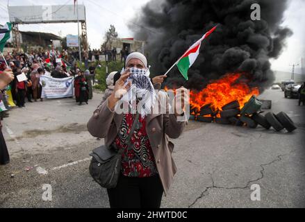 Gaza, Palestine. 07th Mar, 2022. A masked Palestinian woman holds the Palestinian flag during the protest. Ahead of International Women's Day, Palestinian women protested against the Israeli settlements and their expansion in the West Bank, near the Israeli settlement of Homesh in the occupied West Bank. Credit: SOPA Images Limited/Alamy Live News Stock Photo