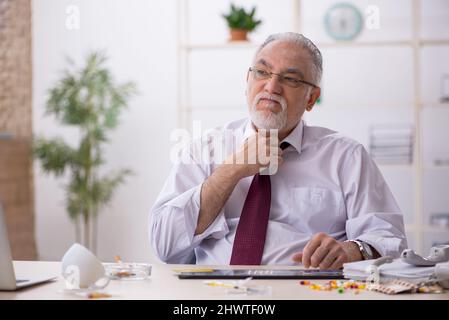 Old male drug addicted employee sitting at workplace Stock Photo