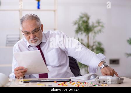 Old male drug addicted employee sitting at workplace Stock Photo