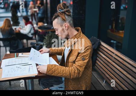 Young man with papers drinking coffee outdoors Stock Photo