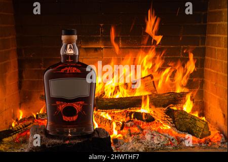 NO LOGO. NO TRADEMARK. View of a bottle of rum, whiskey with a gray empty label on the background of a fireplace fire. High quality photo Stock Photo