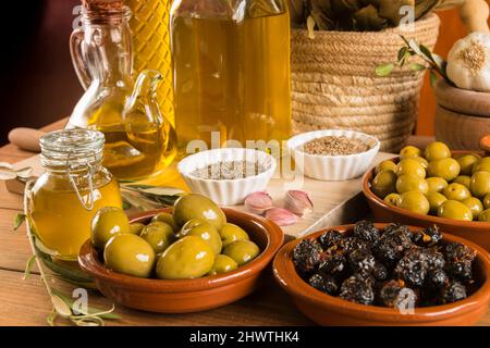 Still life with different varieties of olives seasoned in the traditional way, presented in bowls on wooden boards, and extra virgin olive oil in seve Stock Photo