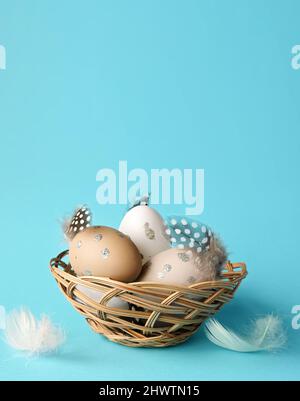 Easter eggs in a nest with feathers on a blue background. Holiday concept. Stock Photo