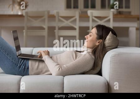Relaxed young woman lying on cozy sofa with laptop Stock Photo