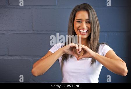 I love you with all my heart. Portrait of a young woman making a heart gesture with her hands against a brick wall background. Stock Photo