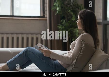 In living room young woman relaxing on couch with book Stock Photo