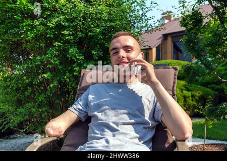 Man with amputated arm talking on the phone sitting on the lawn Stock Photo