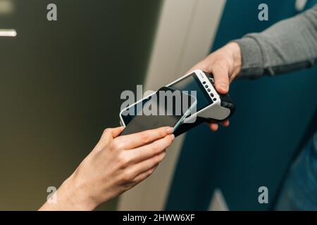 Close-up high-angle view of unrecognizable courier male giving POS wireless terminal to making contactless payment via smartphone to young female Stock Photo