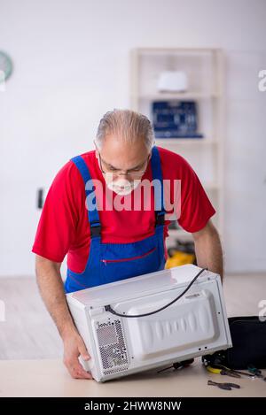 Old male repairman repairing oven at workshop Stock Photo