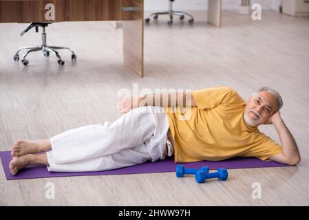 Old boss doing sport exercises during break Stock Photo