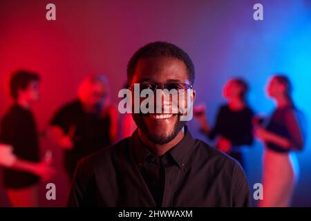 Front view portrait of African American man smiling at camera at party and wearing colored glasses in neon light Stock Photo