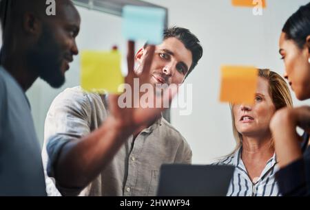 Success is a joint effort. Cropped shot of a group of business colleagues brainstorming on a glass wipe board in their office. Stock Photo