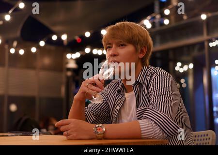 Young Asian man feeling sad and heartbroken after breaking up with his girlfriend while sitting at restaurant Stock Photo