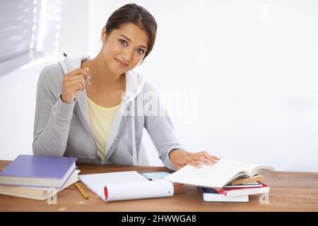 Hitting the books with a positive attitude. A pretty young university student studying for her finals in her dorm room. Stock Photo