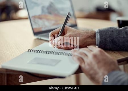 Man writing in spiral notebook and using laptop Stock Photo