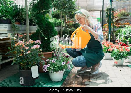 Young woman watering flowers and plants in a garden center Stock Photo