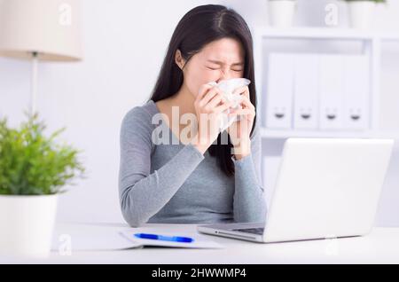 Stressed young  woman sneezing  and working at home office Stock Photo