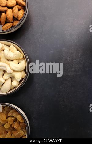Various varieties of nuts and dried fruits are in a bowls on black background. Top view. Healthy food. Vegetarian nutrition. cashew, almond, pistachio Stock Photo
