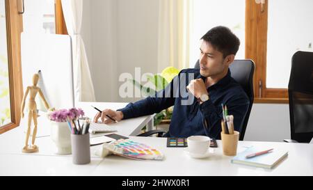 Serious male graphic designer focusing and pensive thinking creative idea on his project in office. Stock Photo