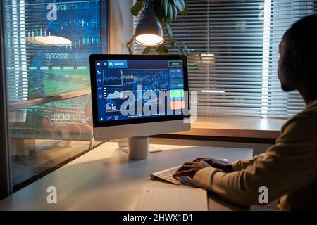 Rear view of African businessman looking at computer monitor and working with software at table at office during deadline Stock Photo