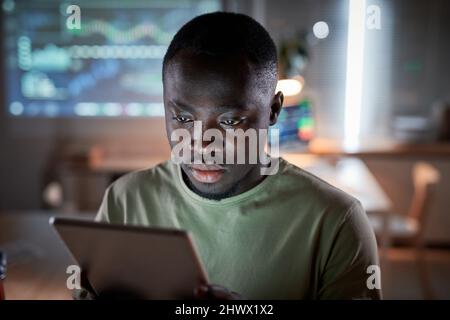 Serious African man looking at the screen of digital tablet during his work at office till late night Stock Photo