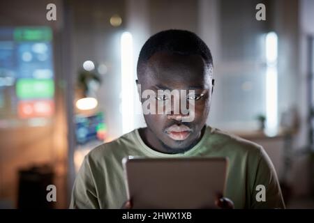 African businessman concentrating on his online work on digital tablet while sitting at office till late night Stock Photo