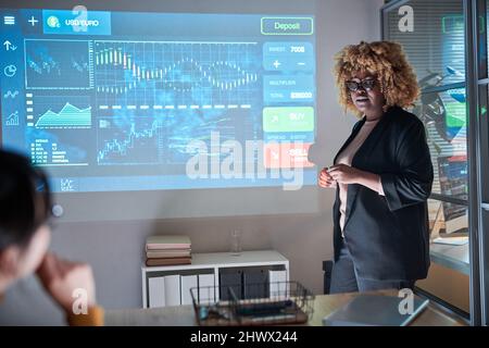 African businesswoman in suit standing near the screen with computer program and presenting her report for colleagues at conference Stock Photo