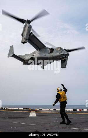 PHILIPPINE SEA (March. 4, 2022) Aviation Boatswain’s Mate (handling) Airman Daunte Babino, from Houston, assigned to the forward-deployed amphibious assault ship USS America (LHA 6), directs an MV-22B Osprey tiltrotor aircraft from the 31st Marine Expeditionary Unit (MEU) to take off from the ship’s flight deck. America, lead ship of the America Amphibious Ready Group, along with the 31st MEU, is operating in the U.S. 7th Fleet area of responsibility to enhance interoperability with allies and partners and serve as a ready response force to defend peace and stability in the Indo-Pacific region Stock Photo