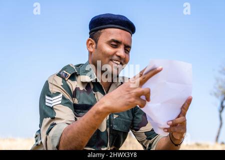 Young indian soldier reading letter or mail from family member while at service on top of mountian - concept of missing family, bonding and distant Stock Photo