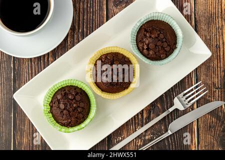 Chocolate chip and cocoa muffins in colorful muffin paper molds on wooden table Stock Photo