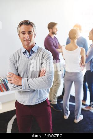 Hes a man with a plan. Portrait of a mature businessman with his colleagues standing in the background. Stock Photo