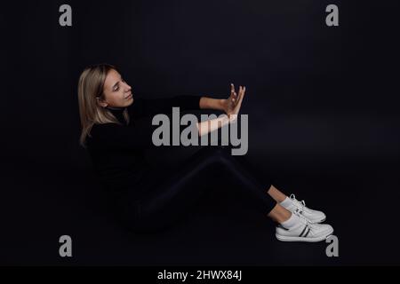 Young Caucasian woman with hands in front of her stopping man from abuse sitting on floor with black background. Domestic physical and psychological Stock Photo