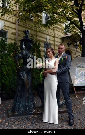 Ukrainian newlyweds posing for a picture by the Pronya Prokopivna and Svirid Holokhvastov sculpture on Andriivskyi descent in Kyiv, Ukraine. Stock Photo