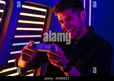 Young bristle man laughing while playing video game with joystick indoors Stock Photo