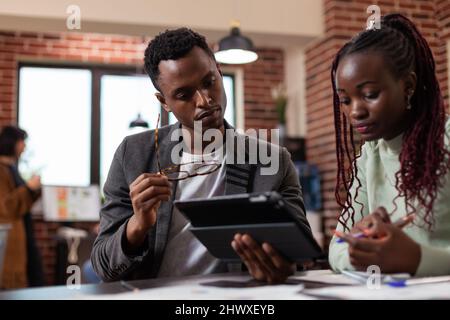 Executive managers analyzing marketing statistics on tablet computer brainstorming ideas for company project during business meeting in startup office. Multiethnic businesspeople planning strategy Stock Photo