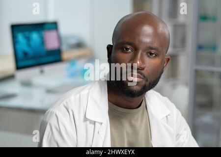 Portrait of serious bearded scientist or chemist in lab coat sitting in front of camera during scientific experiment in laboratory Stock Photo